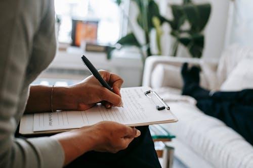 A woman filling out a patient testimonial about her patient experience on a clipboard.